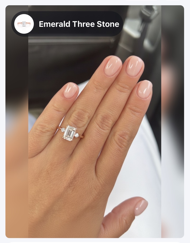 Emerald three stone engagement ring shown on a hand